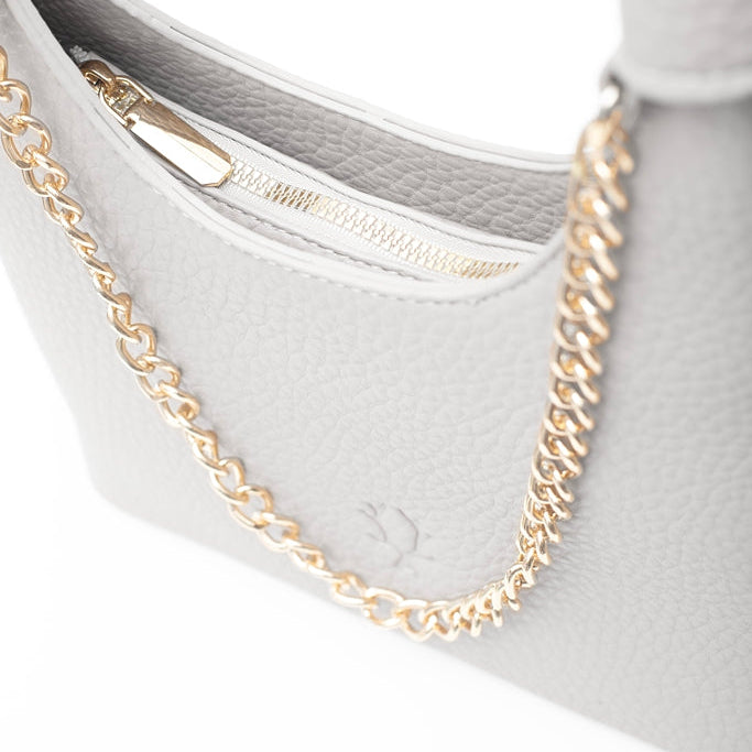Close-up of a light gray pebbled leather handbag with a gold chain strap and gold zipper, 