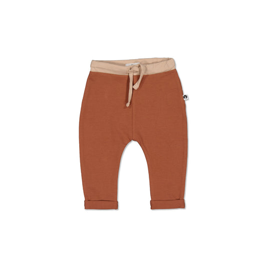 A pair of chestnut-colored baby pants with a fold-over cuff at the ankle and a block colour of latte around the waist. The pants have a drawstring and elastic waist and are made from organic cotton.