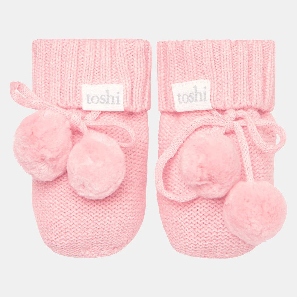 A pair of pink Toshi organic baby booties with ribbed knit cuff and cute pom poms.