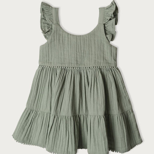 A short-sleeved, green, muslin baby dress with embroidered pompoms and ruffles on the shoulders, featuring a gathered bottom tier.