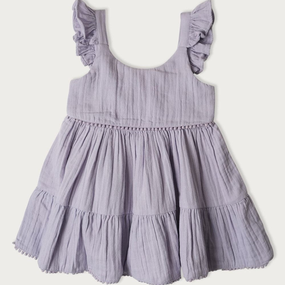 A short summer dress for children, featuring a mixed berry pattern, with pompoms, ruffles on the shoulders, and a smocked panel at the back for easy changing.