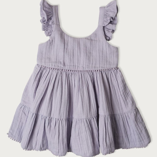 A short summer dress for children, featuring a mixed berry pattern, with pompoms, ruffles on the shoulders, and a smocked panel at the back for easy changing.