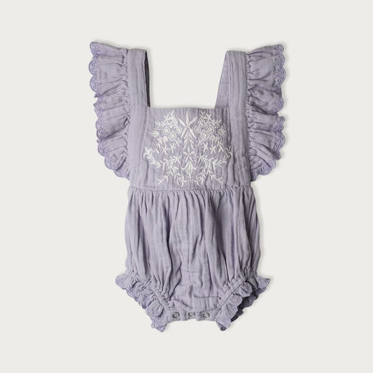 A purple bodysuit with embroidered detailing on the front and ruffle trim, featuring an elastic waistband and adjustable tie at the back