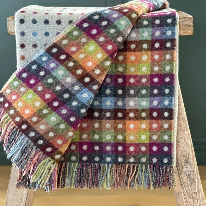 Colorful polka dot wool blanket draped over a wooden chair against a dark green wall.