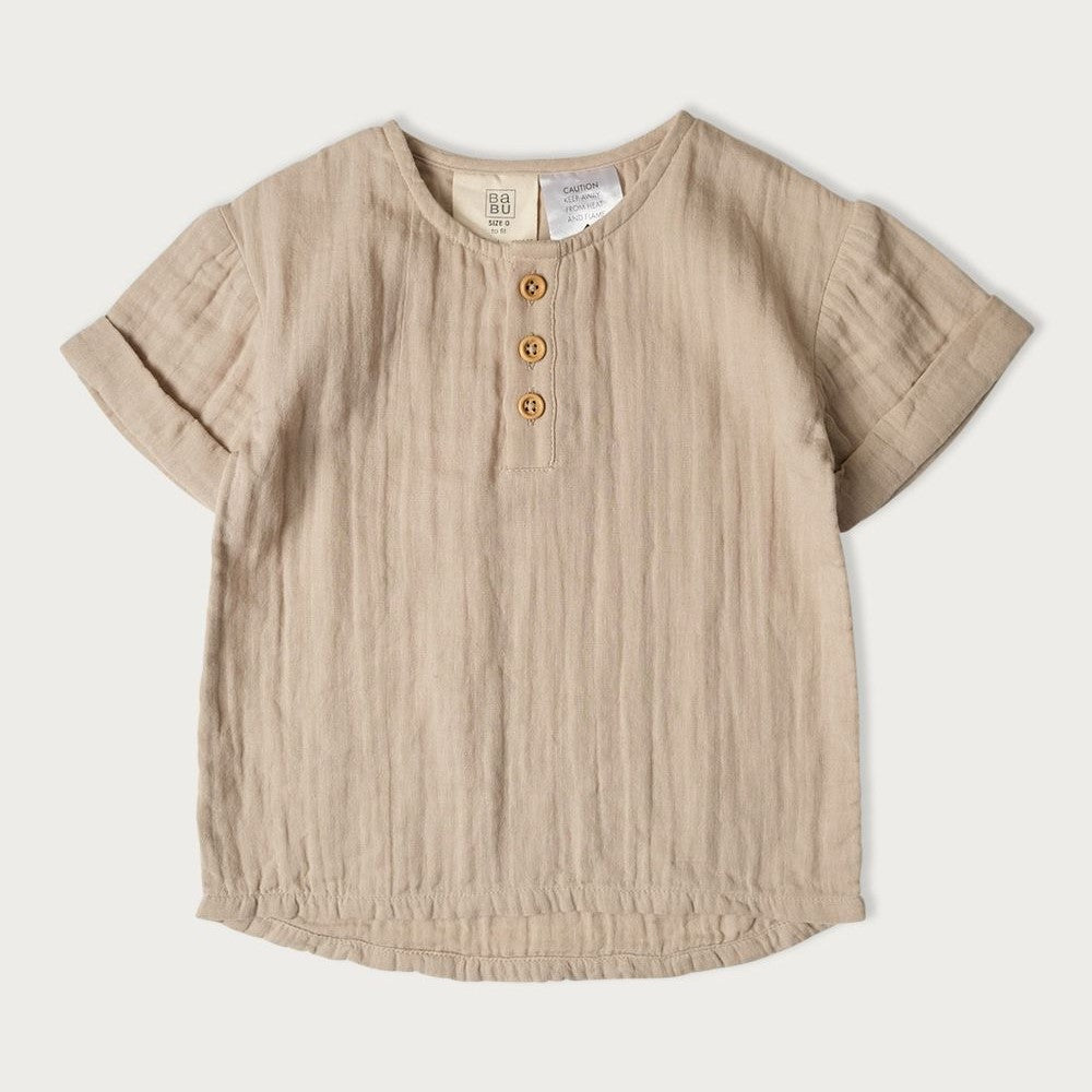 A light beige colored baby shirt with a round neckline, short sleeves, and wooden buttons.