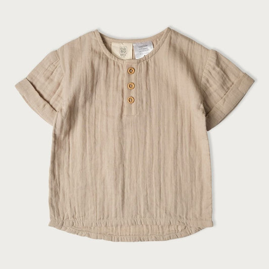 A light beige colored baby shirt with a round neckline, short sleeves, and wooden buttons.