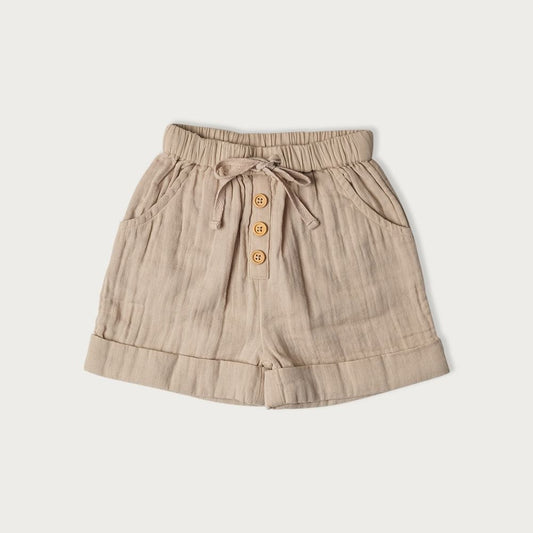 A pair of beige cotton muslin shorts with a tie waistband and wooden buttons for child 