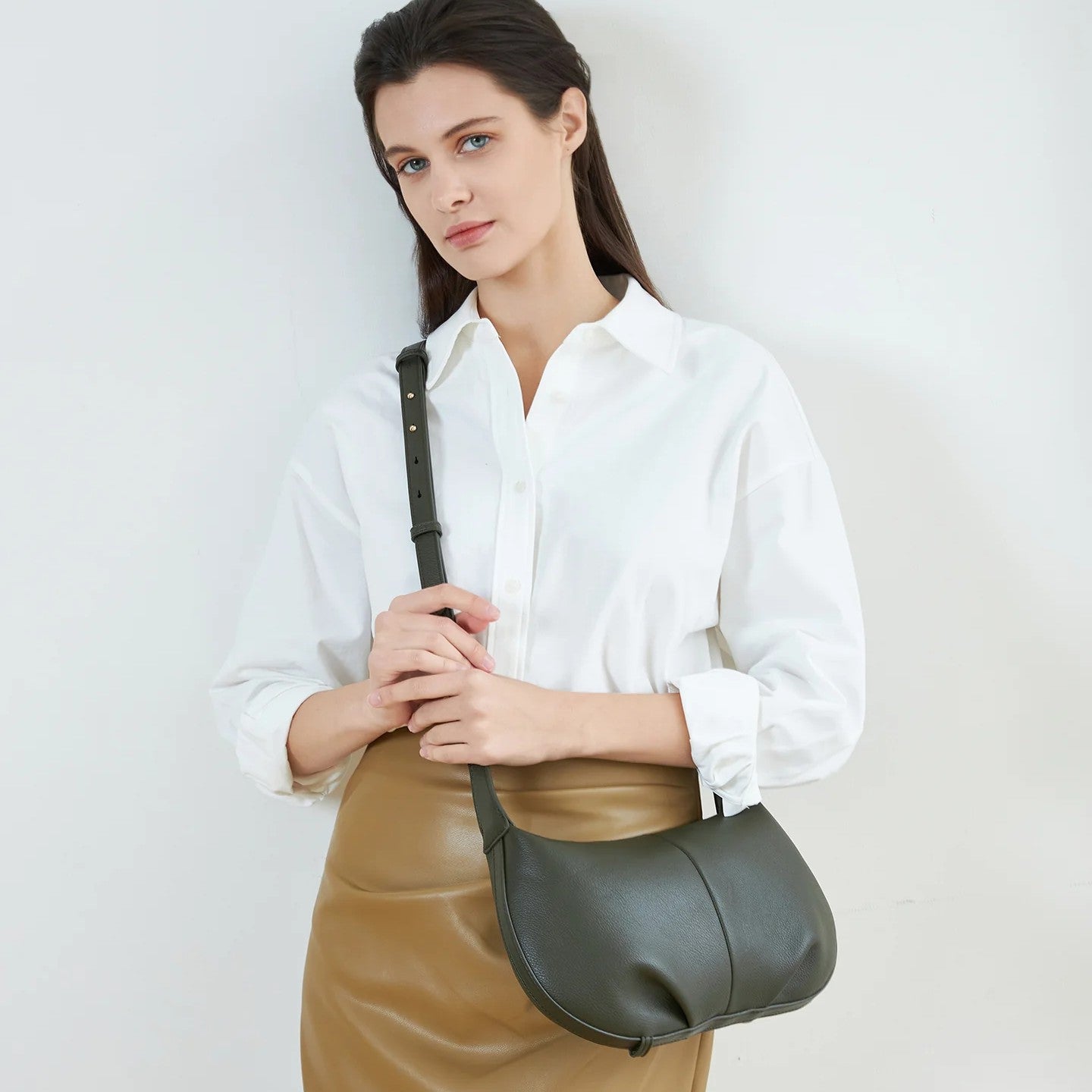 Woman holding a olive green vegan leather cross body bag against a plain background