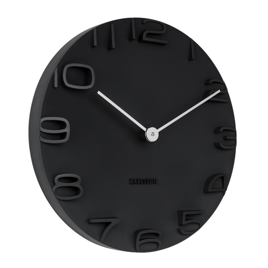 A black wall clock with chrome hands and numbers, branded by Karlsson, with a minimalist open face design.