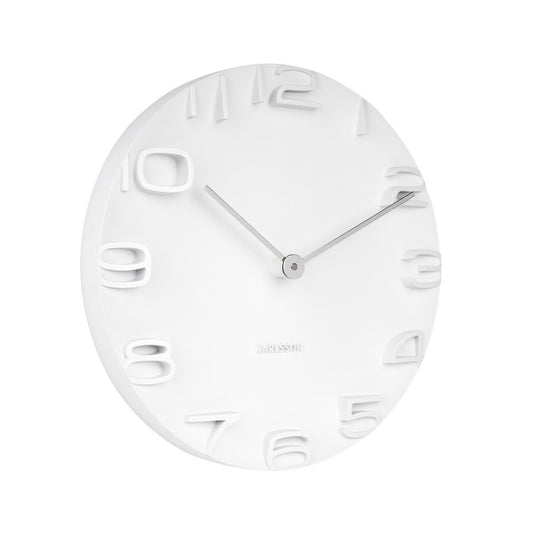 A white wall clock with chrome hands and numbers, mounted on a wall.