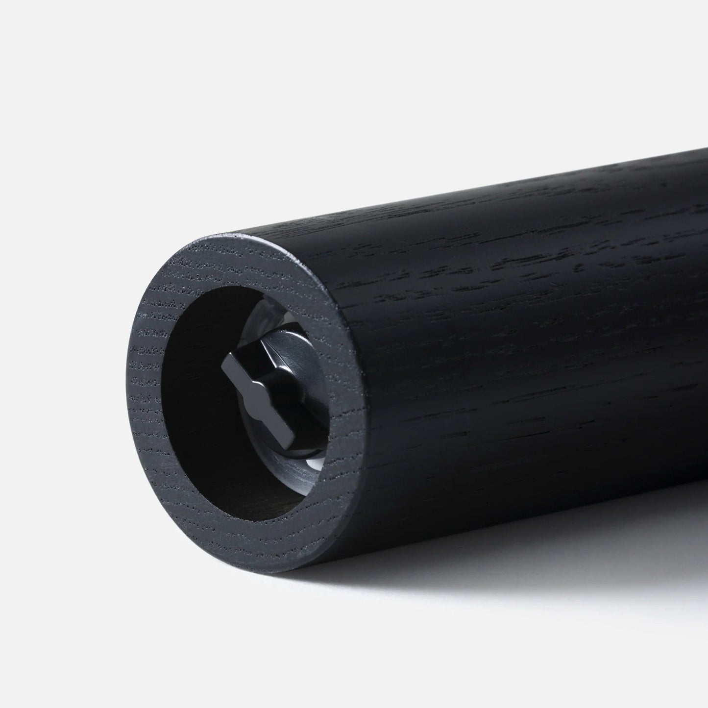 A close-up studio shot of a black cylindrical salt/pepper grinder, likely a rod or handle, showing a circular hollow center with a dark internal component, on a light gray background.