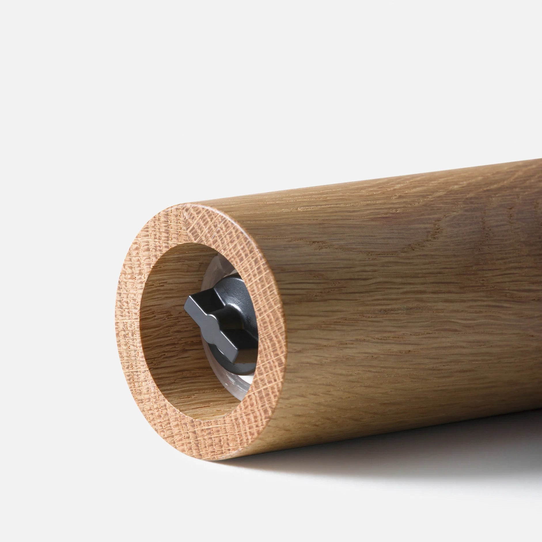 Close-up of a cylindrical wooden rod or handle with a circular hollow center and a visible metallic internal component, photographed on a clean light gray background.