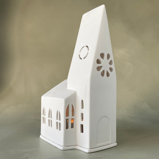 A white porcelain tealight holder designed to resemble a church with a Steeple, window cut-outs, and a flat base. 