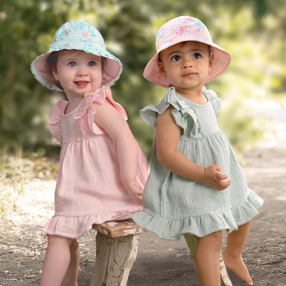 Two young children wearing colorful hats and dresses outdoors.