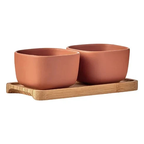 Two terracotta-colored square bowls resting on a light natural bamboo tray, photographed against a solid white background.