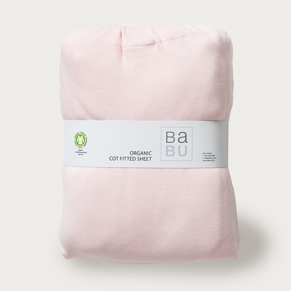 A folded pink fitted cot bottom sheet with a label that reads 'Babu Organic Cotton Sheet'.