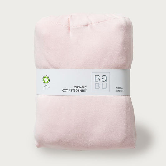 A folded pink fitted cot bottom sheet with a label that reads 'Babu Organic Cotton Sheet'.