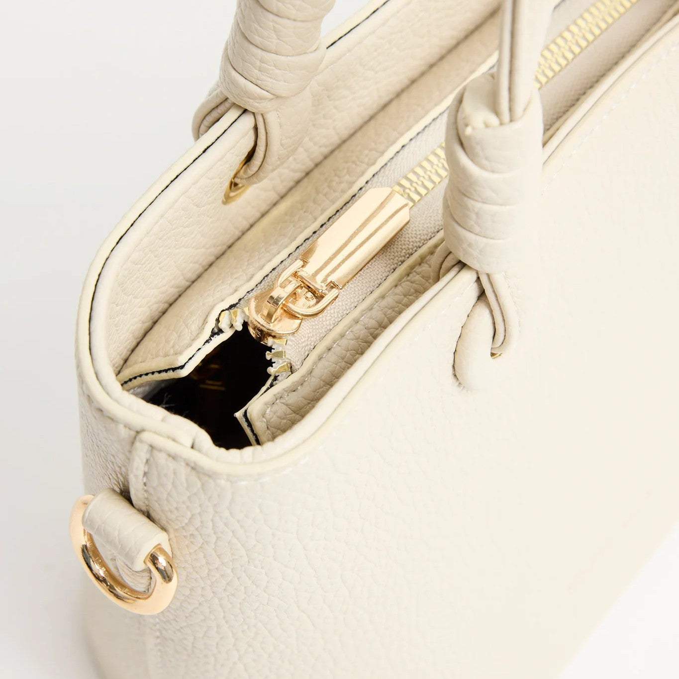 Close-up of a beige handbag with gold zipper and handle on a light gray background