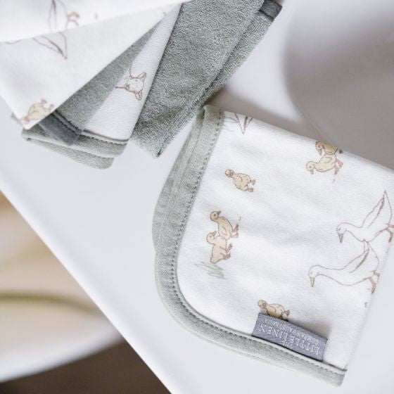 Set of folded sage green baby wash cloths with animal pattern on a white surface