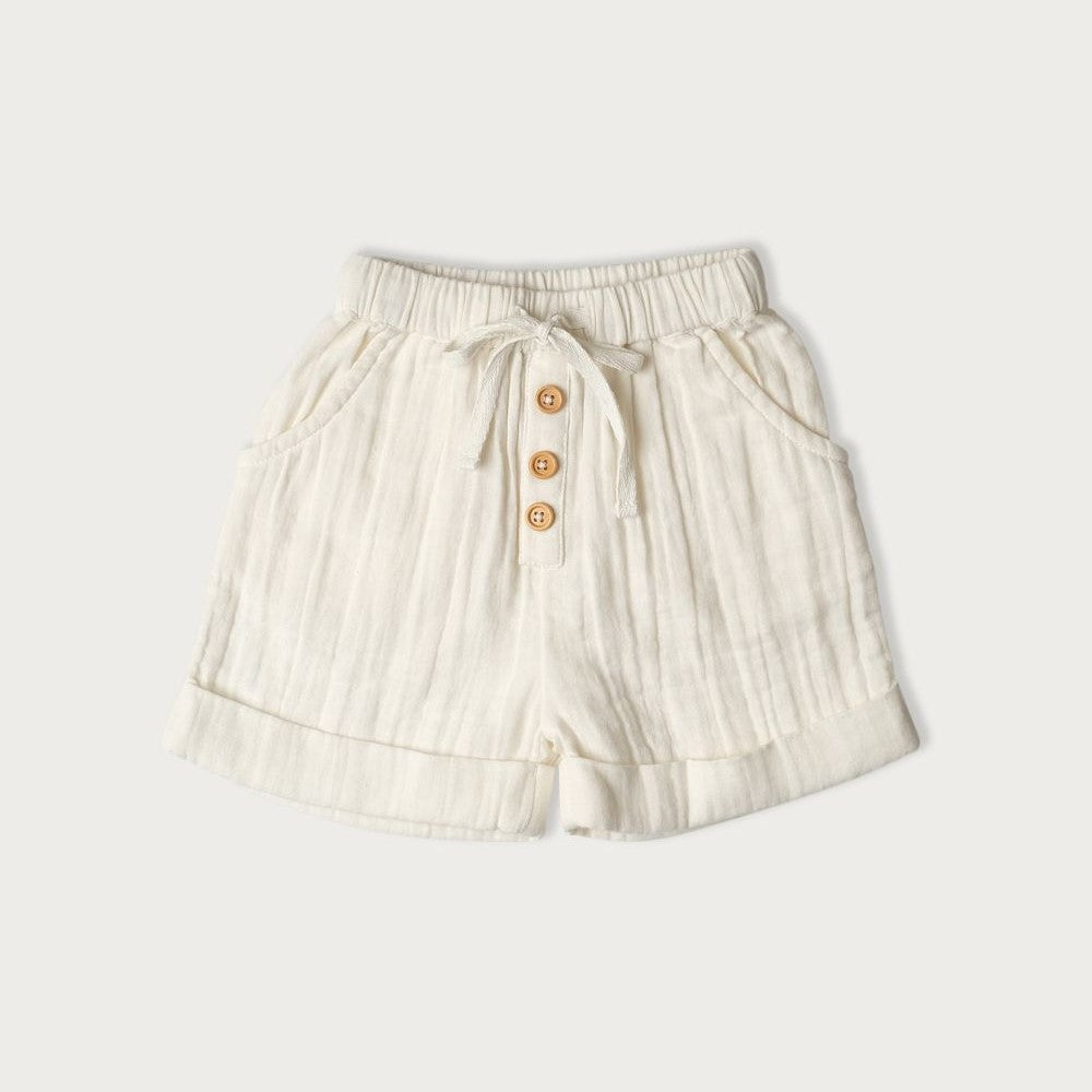 A pair of white muslin short vanilla-colored baby shorts with wooden buttons and a tie waist detail, for child  