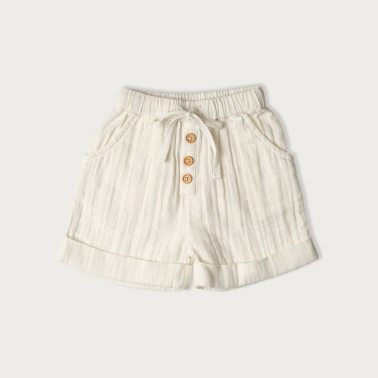 A pair of white muslin short vanilla-colored baby shorts with wooden buttons and a tie waist detail, for child  