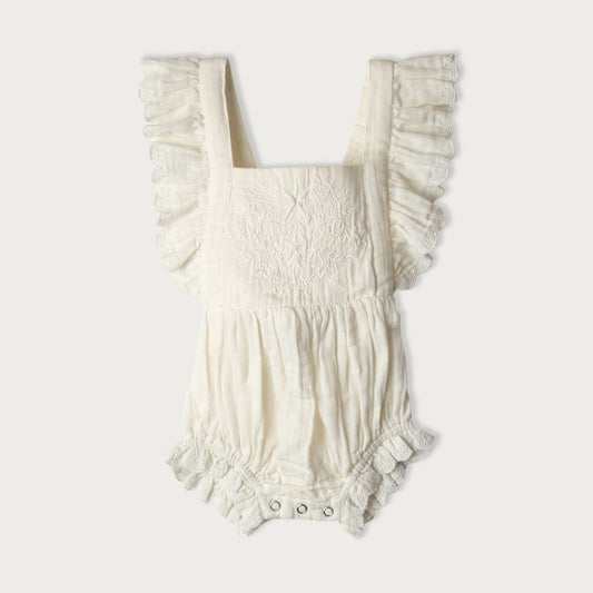A white bodysuit with embroidered detailing on the front panel and ruffles, featuring an adjustable tie up back and an elastic waistband for babies.