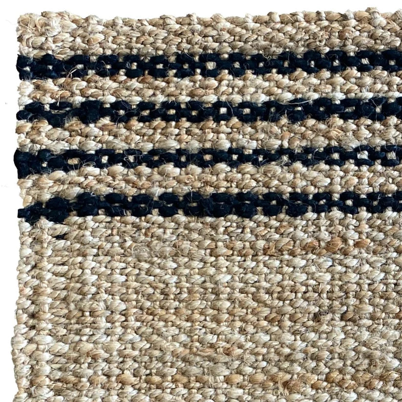 Close-up of a woven rug or textile with a natural beige jute-like texture and three horizontal dark navy stripes.