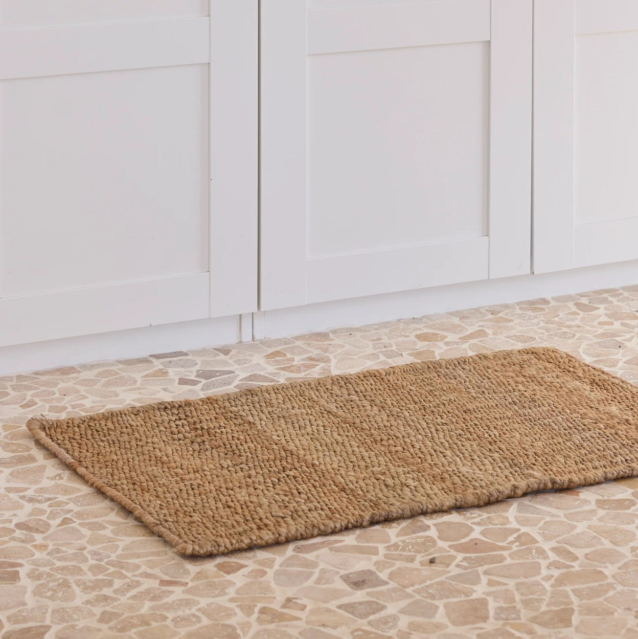 Brown woven mat on a stone floor with white paneled walls.